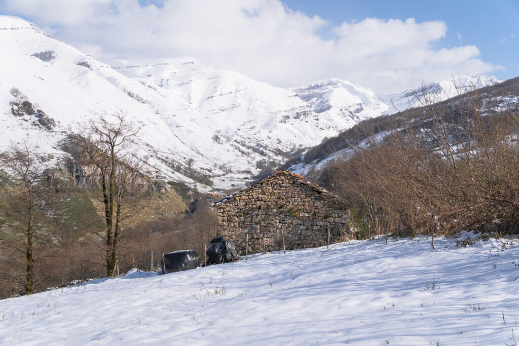 cabaña de piedra con nieve y montañas detrás